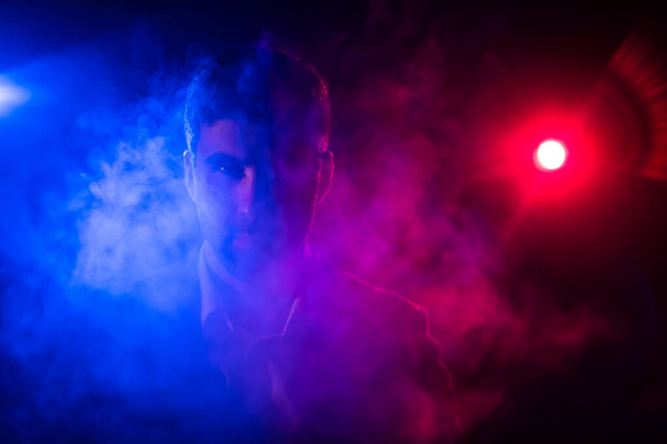 背景の煙とピンクと青の光の中に立つ男の写真. - 写真・画像