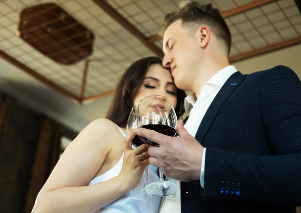 The groom in a suit and the bride in a wedding dress hold glasses of red wine drinking. - Foto, Bild
