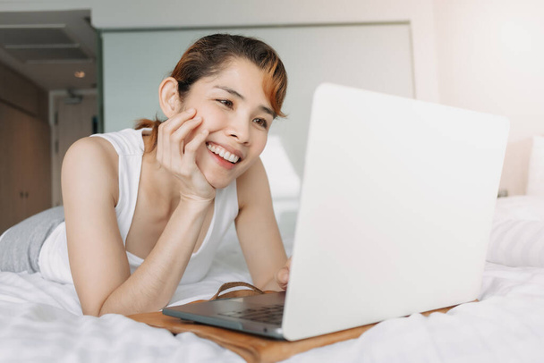 Woman works with laptop on the bed. Concept of work from hotel. - 写真・画像