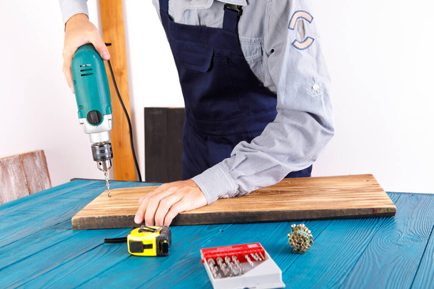 Handyman in blue uniform works with electricity automatic screwdriver. House renovation conception. - Фото, изображение
