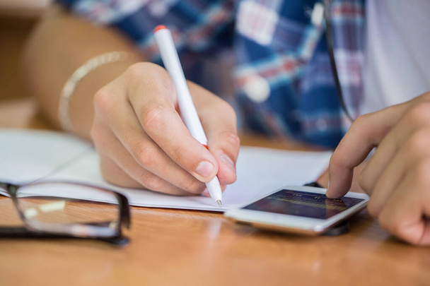 hand on teen writing  on notebook with phone - Fotó, kép