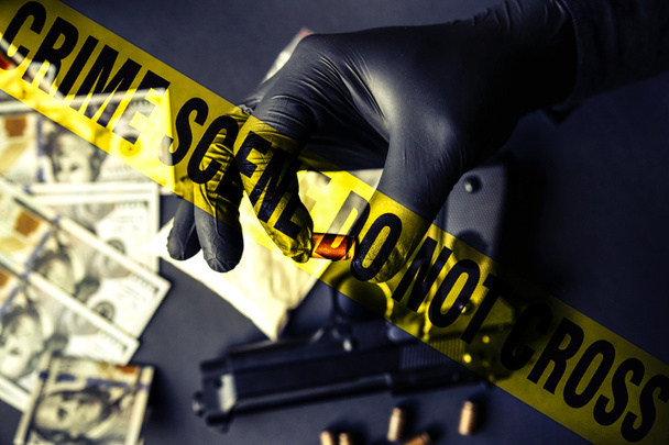 Gun lying on the table. Man in black gloves holding bullets. Illegal drug selling. Criminal problems. Dollars. Police line do not cross tape. - Photo, Image
