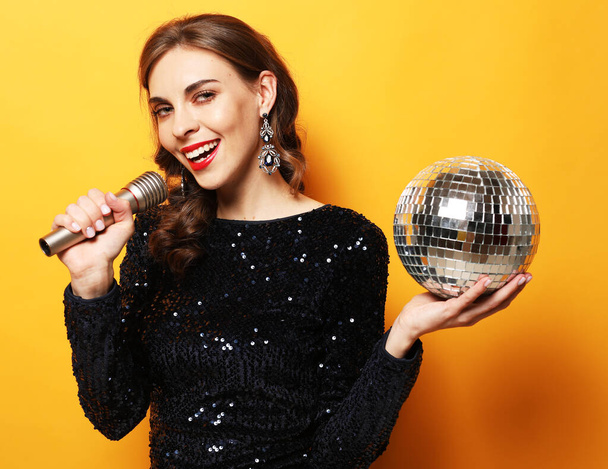 woman in evening dress holding microphone and disco ball. - Фото, зображення
