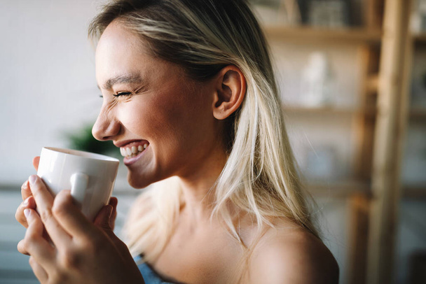 Beautiful young woman enjoying a cup of coffee, tea while relaxing at home. - Foto, afbeelding