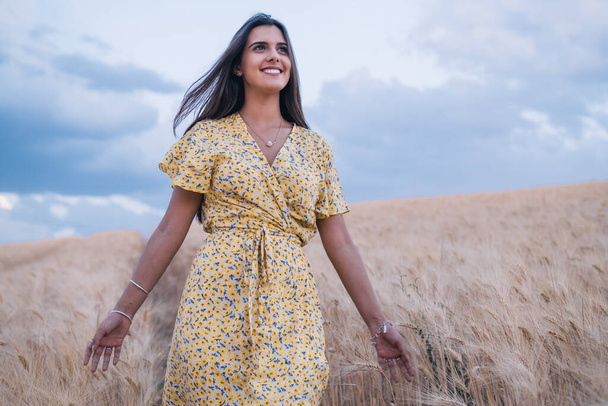 Νεαρή χαρούμενη γυναίκα που απολαμβάνει τη φύση περπατώντας σε ένα χωράφι με σιτάρι. - Φωτογραφία, εικόνα