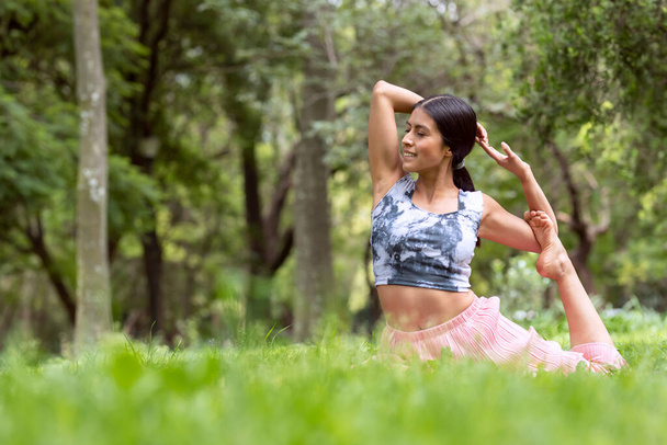 Mexická žena dělá jógu s různými postoji, ve venkovním parku s trávou a stromy v pozadí. - Fotografie, Obrázek