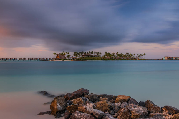 Palmy i budynki na tropikalnym wybrzeżu o zachodzie słońca. Skrzyżowanie Malediwów, hotel hard rock, czerwiec 2021. Obraz długiej ekspozycji - Zdjęcie, obraz