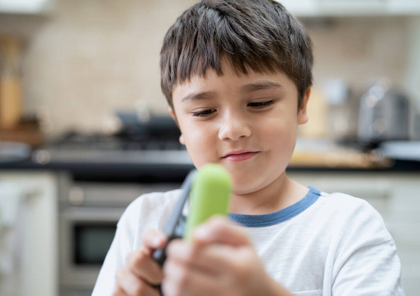 Head shot Young boy crushing fresh garlic into plate, Kid using a garlic press for preparing ingredients for homemade food. candid shot mixed race Child standing in kitchen helping parent cooking food. - Foto, imagen
