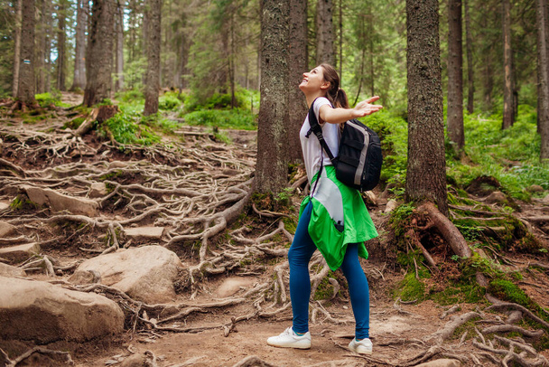 Woman hiker walking through mountain forest path surrounded with roots in Carpathians. Traveler with backpack feels happy. Trip to summer Ukraine - Foto, Imagem