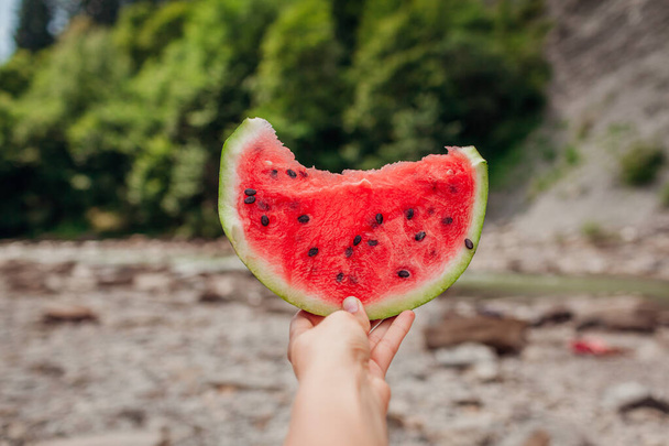 Woman holding piece of watermelon in hand on mountain background outdoors. Snacks eating during traveling in summer. - Photo, Image