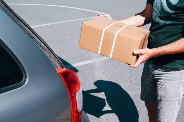 Mladý muž kupce hromadí lepenkové krabice v kufru auta v supermarketu parkoviště. - Fotografie, Obrázek