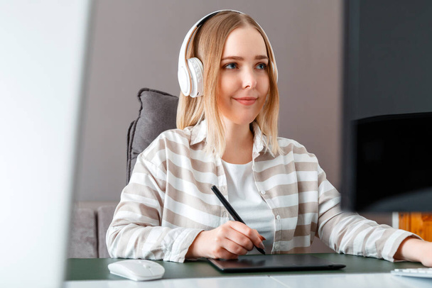 Young woman freelancer designer use graphic tablet while working. Digital artist Woman in headphones works using pc computer At home office. Remote work of illustrator retouchers, designer. - Фото, изображение