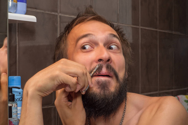 Un hombre con barba se quita el pelo dentro de la nariz - Foto, Imagen