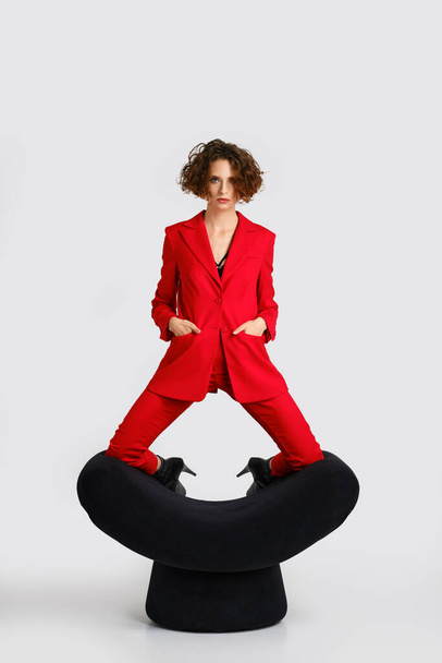 Dancer woman in red pantsui stands on her knees on armrests of a soft armchair  - Foto, afbeelding