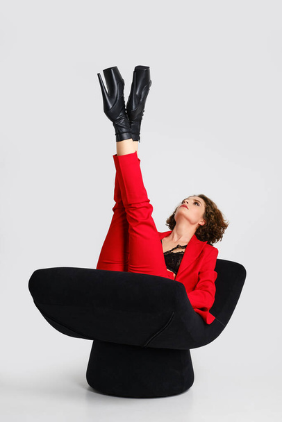 Jovem mulher em pantsui vermelho e botas de dança pólo levantou pernas cruzadas para cima em uma poltrona macia  - Foto, Imagem