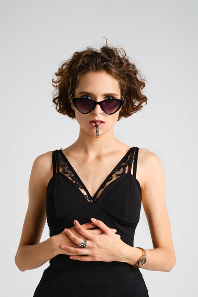 Woman with messy hair and in sunglasses smoking cigarette and holds her hands on stomach - Foto, imagen