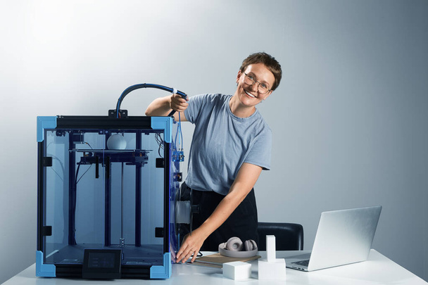 Joven mujer atractiva empresario feliz fijación del tubo en la impresora 3D para hacer prototipo. Preparación para la impresión 3D. Horizontal alta calidad ambiente de trabajo foto imagen. - Foto, Imagen