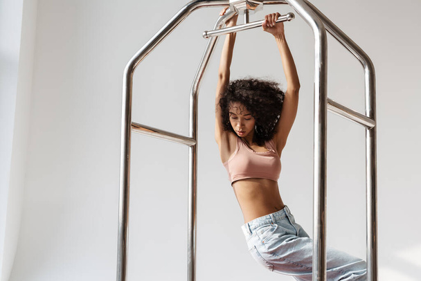 Young african woman wearing brassiere hanging on clothes rail isolated over white wall - Photo, Image