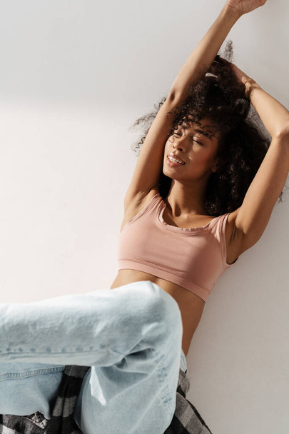 Young african woman wearing jeans smiling while lying on floor isolated over white wall - Foto, immagini