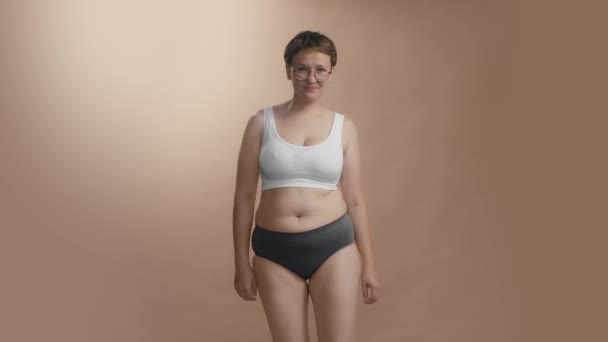 Molesto más mujer de tamaño viendo a sí misma apretando su grasa del abdomen. De alta calidad medio de plano completo de vídeo de estudio. - Metraje, vídeo