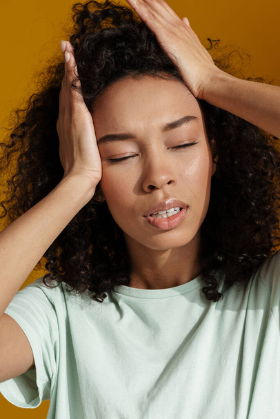 Young african woman wearing t-shirt posing and holding her head isolated over brown wall - Photo, Image