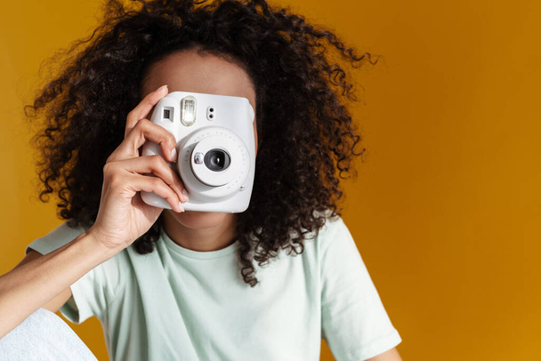 Giovane donna riccia africana indossa t-shirt scattare foto sulla macchina fotografica isolata sopra parete marrone - Foto, immagini