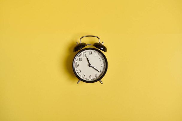 Flache Lagekomposition eines Weckers, auf gelbem Hintergrund mit Platz für Text. Konzept der Kontrolle von Zeit, Zeitmanagement, Business und Veranstaltungen - Foto, Bild