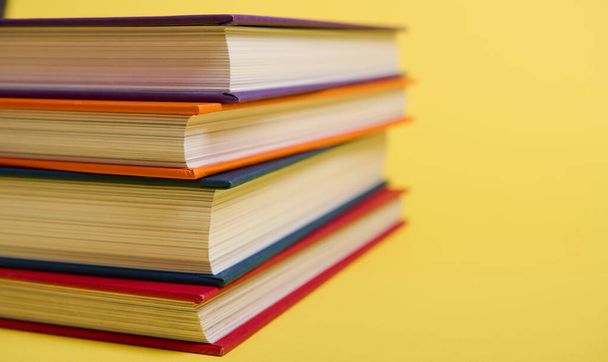Close-up of a stack of multicolored books on yellow surface background with copy space for text. Teacher's Day concept, Knowledge, literature ,reading, erudition - Fotografie, Obrázek