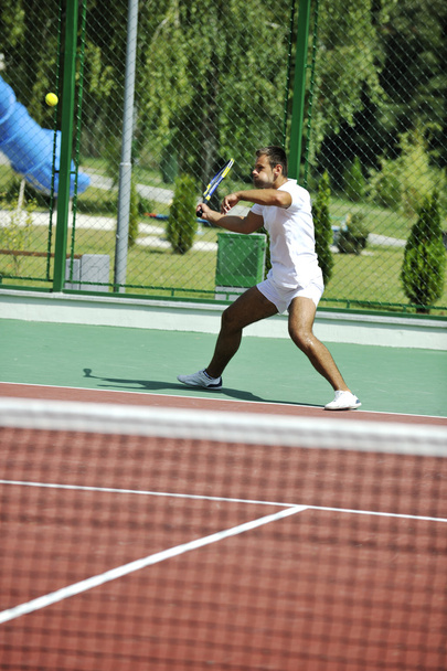 Young man play tennis outdoor on orange tennis court at early morning - Foto, imagen