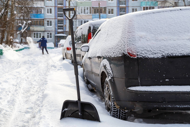 пластиковая снежная лопата перед покрытой снегом машиной в солнечное зимнее утро - Фото, изображение