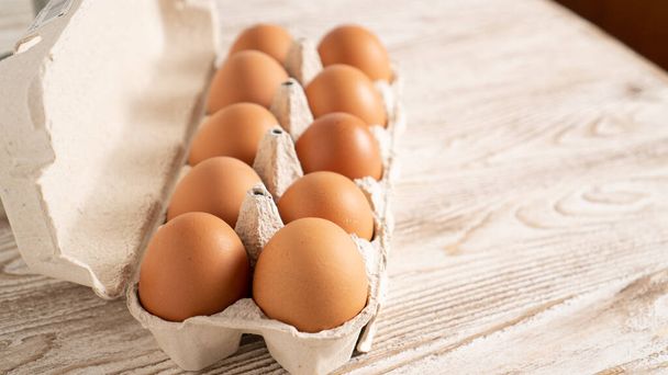 Barna tyúktojás az asztalon. 10 tojást tartalmazó csomag. Friss tanyasi tojás kartondobozban, fa alapon. - Fotó, kép