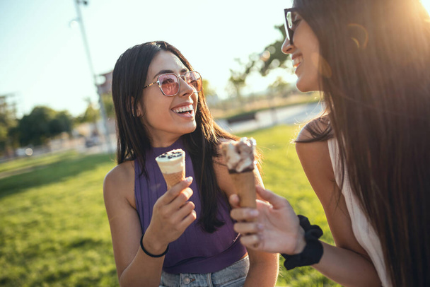 Shoot of two beautiful young women eating ice cream while having fun walking through the park in the city. - Fotoğraf, Görsel