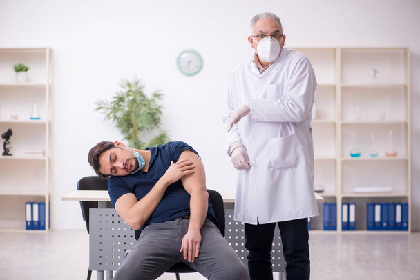 Jeune patient de sexe masculin visitant un vieux médecin en conce de vaccination - Photo, image