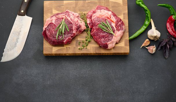 raw piece of beef ribeye with rosemary, thyme on a black table, top view, copy space - Foto, immagini