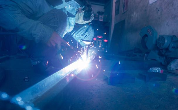 Welder welding metal with argon arc welding machine and has welding sparks. A man wears welding mask and protective gloves. Safety in industrial workplace. Welder working with safety. Steel industry. - Photo, Image