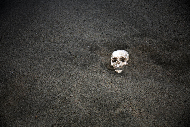 Halloween. HUMAN SKULL in Verbindung setzen. Menschlicher Schädel an einem Strand angespült. Menschlicher Schädel im Sand vergraben Ozean mit menschlichem Schädel im Sand mit Wellen und Meerschaum. Beängstigende menschliche Knochen auf antiken archäologischen Stätten. Schädel im Sand am Meer begraben. - Foto, Bild