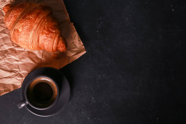 Frissen sült croissant kézműves papíron, egy bögre expresso sötét betonasztalon. Egy csésze forró kávét, zsemlét, zsemlét. Kaja, francia reggeli, reggeli menü, kávézó koncepció. Felülnézet, másolás - Fotó, kép