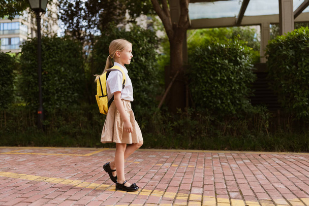 Schoolgirl back to school after summer vacations. Child in uniform smiling early morning outdoor.  - Photo, image