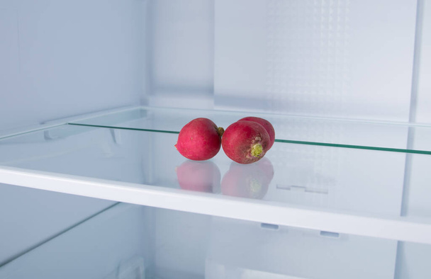 against the background of a white refrigerator, there is a red radish on a glass shelf, close-up - Photo, image