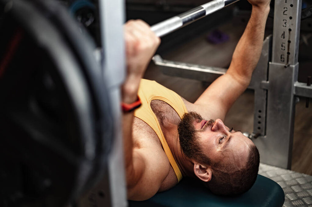 Bearded man bodybuilder doing bench press exercise in gym - Photo, Image