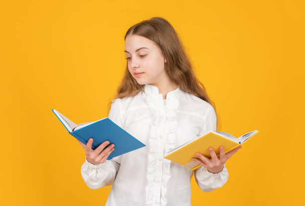 serious kid in white shirt ready to study do homework reading book on yellow background, literature - Zdjęcie, obraz