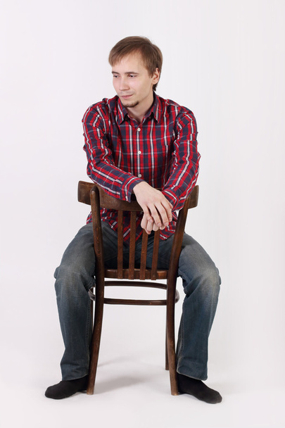 Young man with beard in checkered red shirt sits astride chair a - Fotoğraf, Görsel