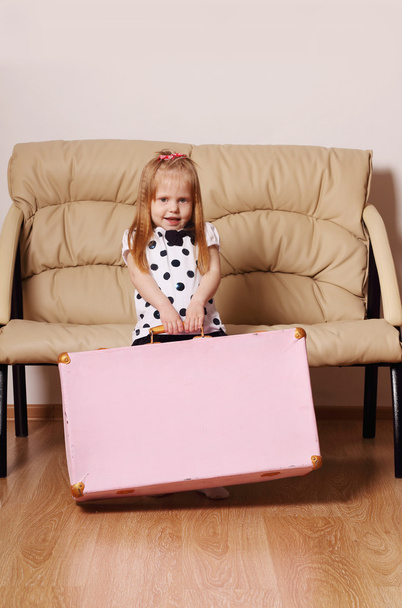 Pretty little blonde girl drags big pink suitcase near sofa in r - Foto, Imagem