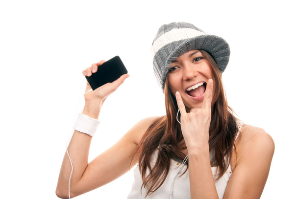 Pretty rock girl showing cellular mobile phone and in rock n roll sign finger smiling in headphones and hat isolated on a white background. - Foto, immagini