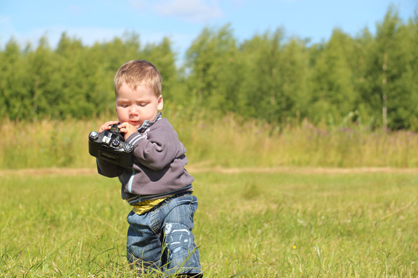 Little handsome boy holds camera and walks at meadow in summer d - Foto, afbeelding