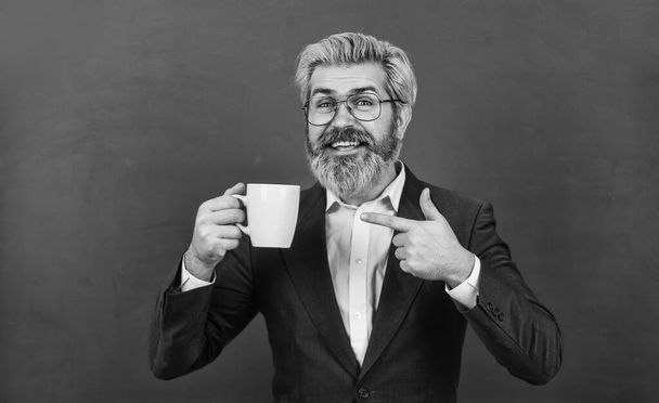 This morning is sponsored by coffee. Happy teacher point at tea cup. Bearded man drink morning coffee. Morning and breakfast. Old school energy drink. School break. Morning cup of good mood - Foto, Imagem