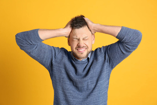Man suffering from terrible migraine on yellow background - Photo, image
