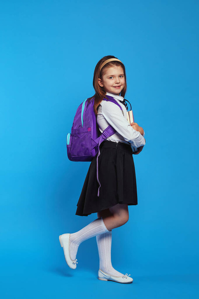 Colpo verticale di ragazza che indossa zaino e uniforme scolastica, in possesso di libri - Foto, immagini