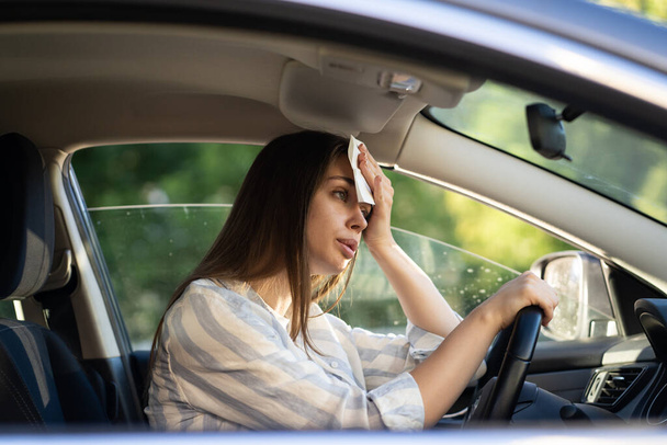 Vrouw bestuurder heet tijdens hittegolf in de auto, die last heeft van warm weer veegt zweet van het voorhoofd - Foto, afbeelding
