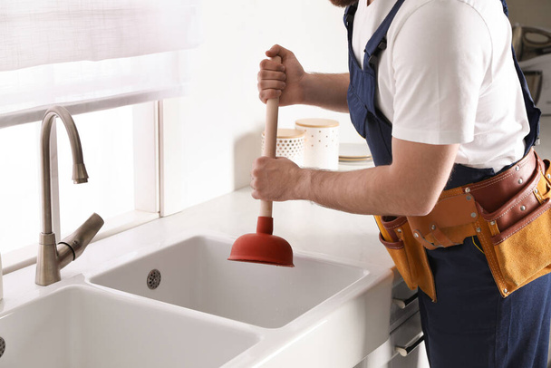 Plumber using plunger to unclog sink drain in kitchen, closeup - Photo, Image
